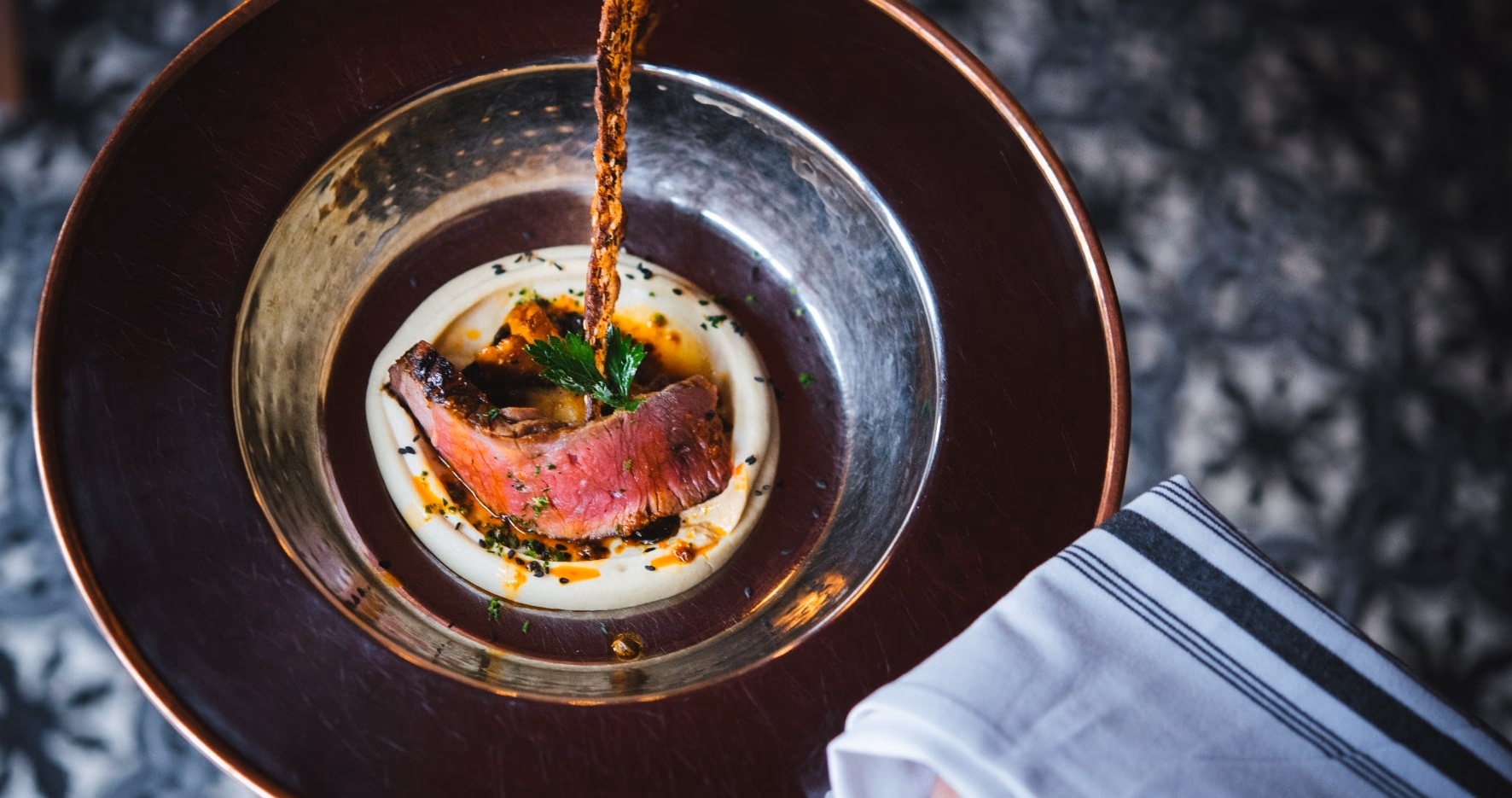 Pièce de bœuf grillée sur purée, servie dans un plat de cuivre martelé.